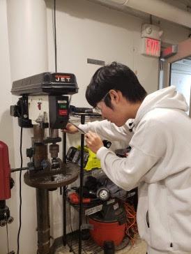 Terry '24 using the drill press on a mechanical project.