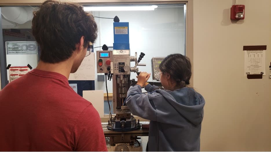 Owen '25 teaching Sharon '27 how to use the mill which drills holes with precise measurements into our aluminum.