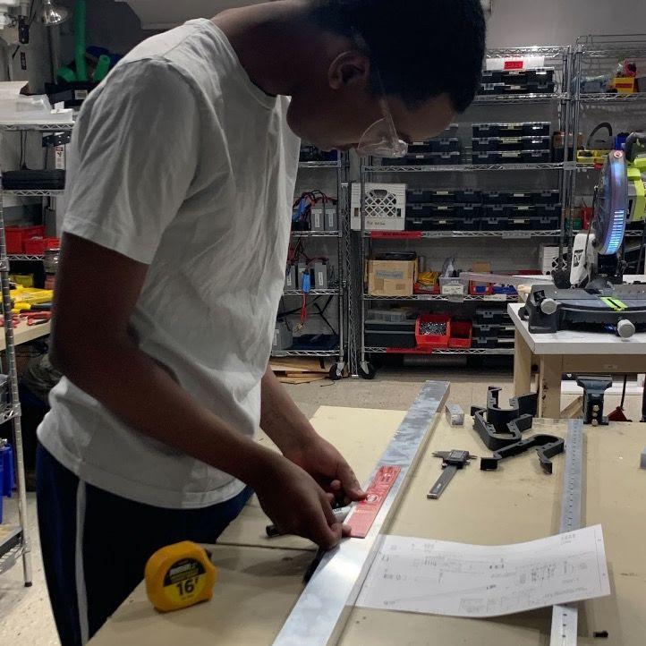 Zach '25 measuring and marking up a 2 by 1 metal tube before cutting it.