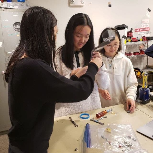 Sophia '25, Ally '25, and Kendree '25 making a small catapult at the first Mechanical training.